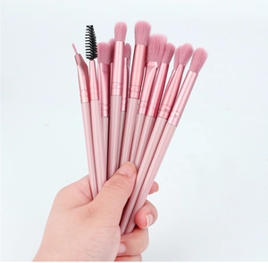 Hand holding set of 11 pink makeup brushes with synthetic bristles and wooden handles