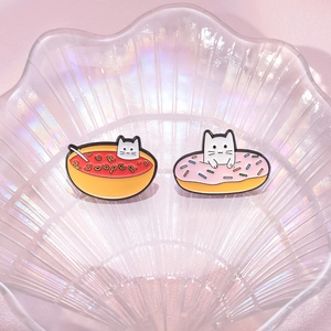 Cute cat enamel pins in soup bowl and donut shapes on a decorative glass tray