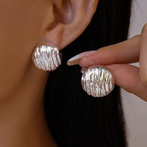 Détail des boucles d'oreilles rondes en métal argenté avec une surface plissée texturée