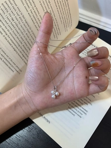 Detailed shot of a three-pearl cluster pendant on a delicate silver chain held in hand