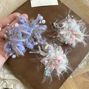 Detail of handmade knit flower earrings with pearl accents held in hand for size context