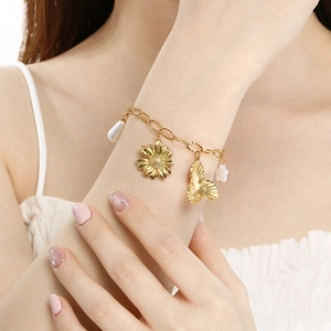 Golden bracelet featuring sunflower, butterfly, and pearl charms worn on wrist
