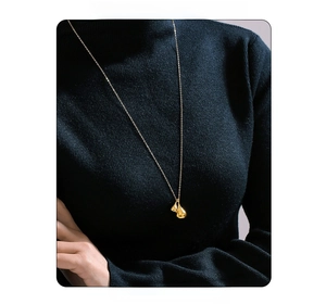 Golden teardrop double pendant necklace on dark sweater background with fashion text