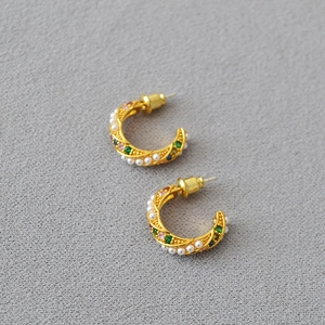 Close-up of golden C-shaped earrings featuring white pearls and colorful zircon stones