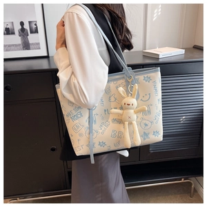 Detailed close-up of a cream graffiti tote bag with a plush bunny charm on a shoulder