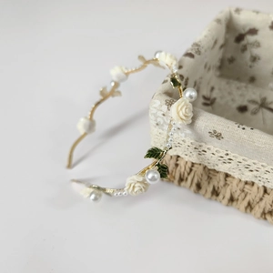 Detailed view of golden headband with white resin roses, green leaves and pearls on basket