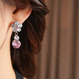 Detailed close-up of a zircon floral drop earring with a pink stone on a model