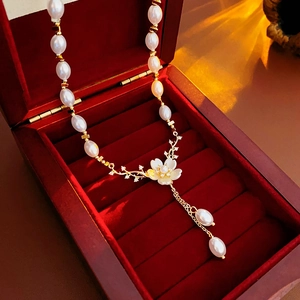 Détail d'un collier de perles avec pendentif fleur et pompons dans un écrin en velours rouge