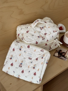 Detailed set of two quilted circus bear makeup bags with a bow zipper on a wooden background