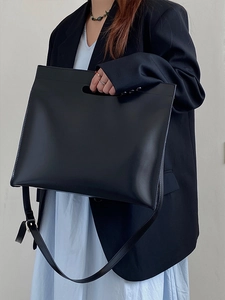 Close-up of minimalist black leather tote bag with hollow handle and long strap
