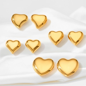 Macro detail of four pairs of golden heart-shaped stud earrings on white silk fabric