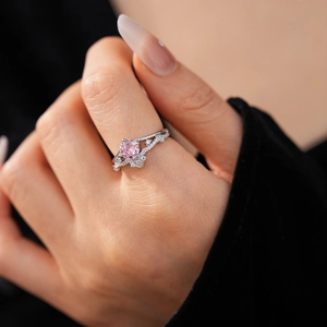 Close-up of elegant crown ring with pink zircon and wavy band on woman's finger