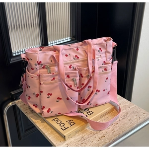 Detail of pink cherry print tote bag with multiple zip pockets on a marble surface