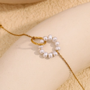 Detailed view of 18K gold double ring bracelet featuring white pearls on a textured background