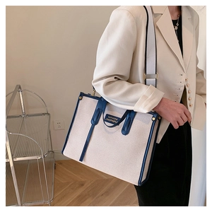 Detail of canvas tote bag with contrast blue trim and branded gold embossed front label