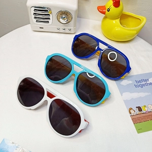 Three pairs of colorful round-frame kids sunglasses arranged on a white surface with props