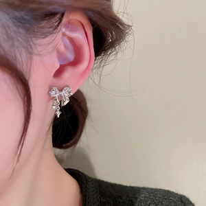 Detailed view of silver bow earrings with zircon star pendant worn on ear