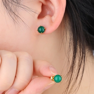 Close-up of a green round gemstone stud earring with 18k gold plating on a model ear