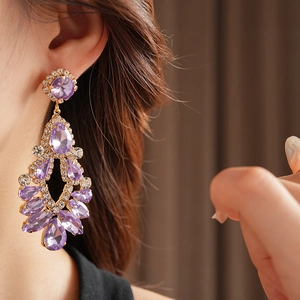 Close-up of golden teardrop tassel earrings with purple gems and sparkling rhinestones