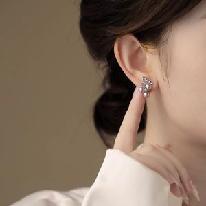 Elegant floral pearl stud earrings with silver diamond accents worn by a model