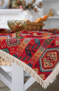 Close-up of red ethnic jacquard tablecloth with beige tassels on a white wooden table