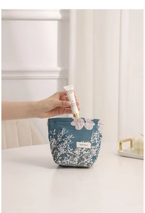 Detailed close-up view of hand placing cream into a floral jacquard makeup bag pouch