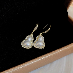 Detailed macro view of golden gourd earrings with white stones in a black velvet box