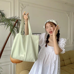 Detailed view of spacious light green canvas tote bag with wide shoulder strap on a model