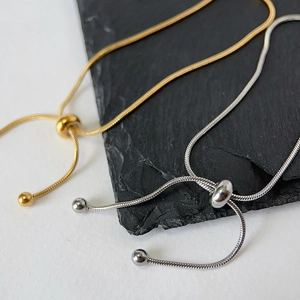 Adjustable snake bone chain bracelets in 18k gold and silver finish on a rock surface