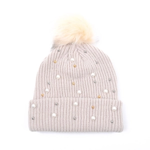 Dettaglio di cappello in maglia con pompon di pelliccia, perle bianche e dorate