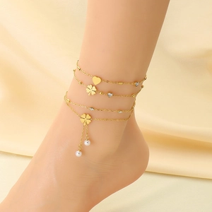 Close-up of golden layered anklet featuring heart charms, clover petals and white pearls