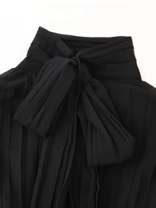 Close-up of pleated high-neck detail with black chiffon bow tie on commuting dress