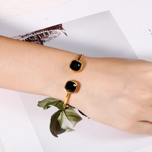 Detail of gold open cuff bracelet featuring square black stones on a model's wrist