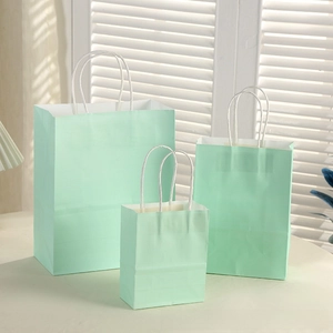 Three mint green paper gift bags in various sizes with white woven handles on a white table
