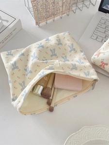 Floral canvas makeup bag with blue bow prints and smooth zipper closure in a desk setting