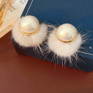 Close-up of white pompom pearl earring with gold rim on a dark blue jewelry box