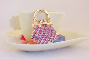 Close-up of golden handbag charm with pink and white rhinestones on a heart cup