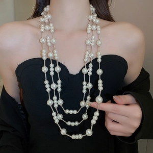 Detail of elegant multi-layer pearl necklace on a model with white faux pearls and thin chains
