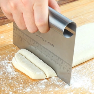 Stainless steel dough scraper with scale measuring dough on a wooden board