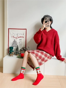 Detail shot of red Christmas thermal socks with elk patterns worn by a model in a cozy scene