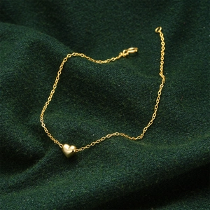 Detail shot of heart pendant on a gold chain bracelet over green fabric background