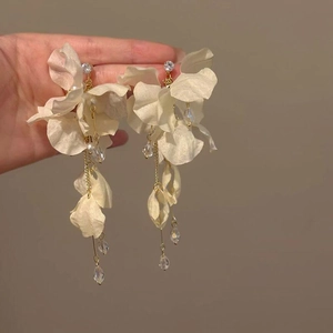 Detailed view of oversized white fabric flower earrings with elegant long golden tassels.