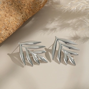 Detailed view of silver leaf-shaped earrings on a natural stone and beige surface