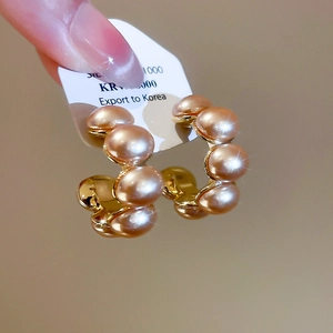 Detailed macro of C-shaped gold-plated pearl earrings with polished champagne finish