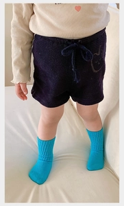 Toddler in navy knit shorts and bright blue knee-high socks on a soft indoor sofa