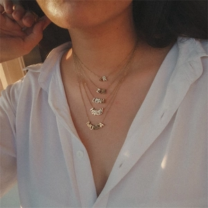 Model wearing layered gold stainless steel name necklaces with multiple letter pendants