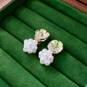 Macro view of floral pearl earrings with iridescent petals on a green velvet tray