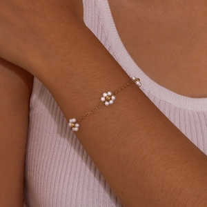 Close-up of gold stainless steel bracelet with three pearl flower charms on a female wrist