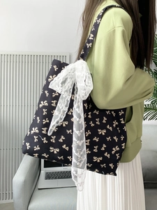 Black canvas tote bag with beige bow print and large white lace bow detail for casual use