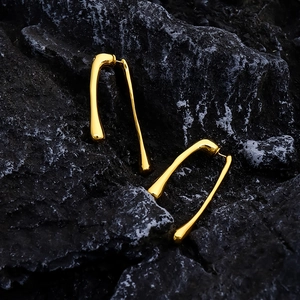 Macro shot of long gold-plated liquid drop earrings on a black textured stone background